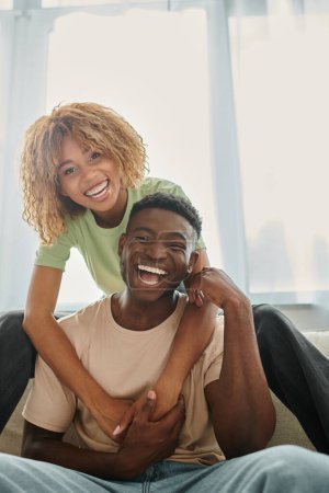 joyful african american woman embracing boyfriend in living room, black couple and quality time