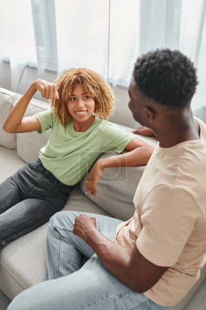 happy black woman in braces sitting on sofa and looking at boyfriend, nonverbal communication