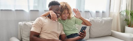 happy african american couple video chatting on a smartphone while sitting on couch together, banner