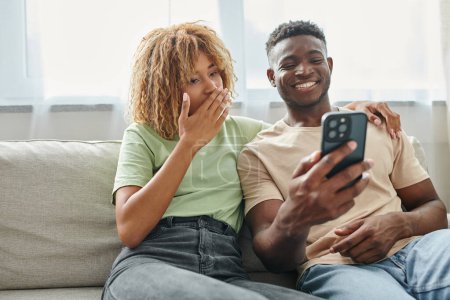 glücklich afrikanisch-amerikanisches Paar lacht, während Video-Chat auf einem Smartphone zu Hause, Kommunikation