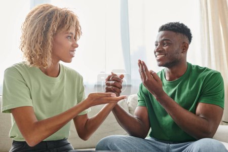 heureux couple afro-américain communiquant avec la langue des signes tout en étant assis sur le canapé