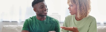 feliz pareja afroamericana que se comunica con el lenguaje de signos mientras está sentado en el sofá, pancarta