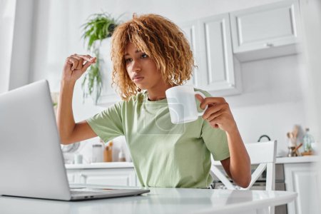 serious african american woman using sign language during video call and holding cup, nonverbal