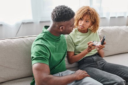 deaf african american woman holding hearing aid in a box near boyfriend while sitting on couch