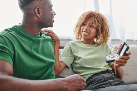 heureuse femme afro-américaine dans des bretelles tenant boîte avec appareil auditif dispositif médical près du petit ami
