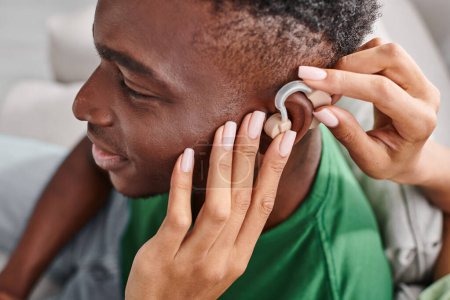 erfreut afrikanisch-amerikanischer Mann lächelt, während seine Freundin mit Hörgeräten, medizinischen Geräten hilft