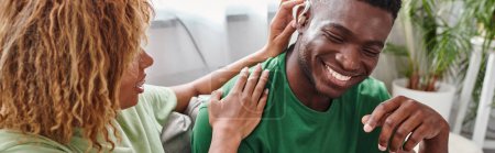 homme afro-américain souriant que sa petite amie bouclée aide avec l'aide auditive, bannière horizontale