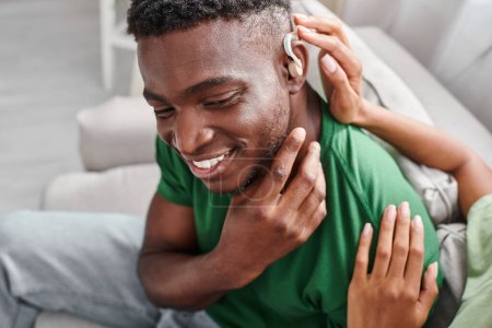deaf african american man smiling as his girlfriend assists with hearing aid, medical device