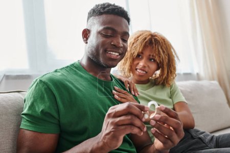 happy african american man holding hearing aid medical device near girlfriend, listening device