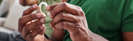 Photo for Cropped banner of hearing aid in hands on black man, african american person holding medical device - Royalty Free Image