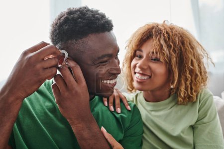 deaf and happy african american man wearing hearing aid near girlfriend, health device
