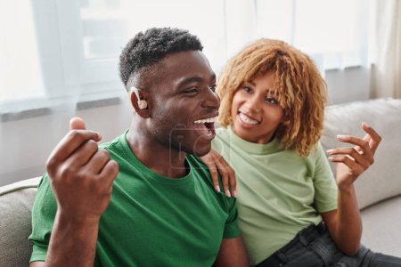 excité homme afro-américain dans l'appareil auditif assis près de petite amie heureuse dans les bretelles