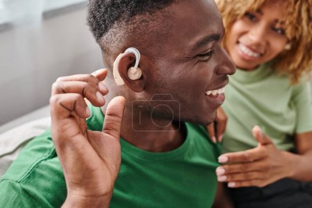 excité homme afro-américain dans l'appareil auditif assis près de petite amie floue dans les bretelles