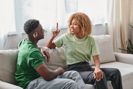 Pareja afroamericana que se comunica con el lenguaje de señas en el sofá, hombre negro en audífono