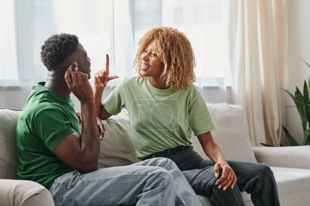 Pareja afroamericana que se comunica usando un lenguaje de señas en el sofá, hombre negro en audífono