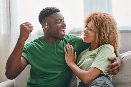 pareja afroamericana emocionada abrazando, hombre negro sordo en audífono y mujer en aparatos ortopédicos