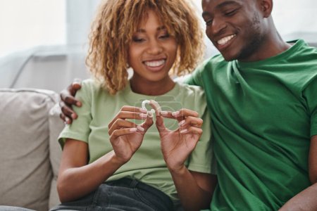 happy african american couple holding hearing aid medical device near boyfriend, accessibility