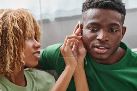curly african american woman holding hearing aid medical device near boyfriend, accessibility