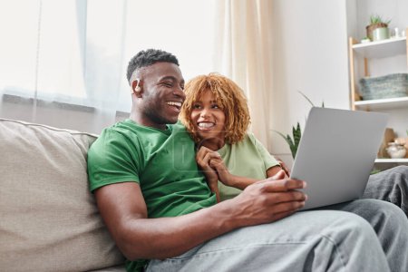 joyful african american couple walking movie on laptop, deaf man in hearing air and woman in braces