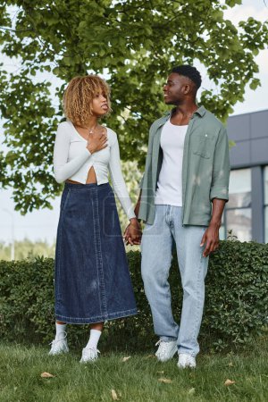 Téléchargez les photos : Heureux couple afro-américain tenant la main et communiquant avec des gestes à l'extérieur - en image libre de droit