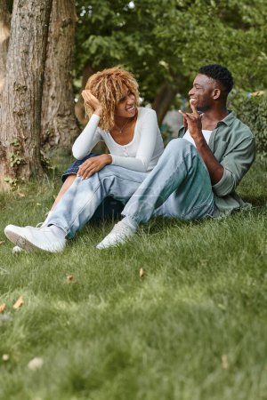 Téléchargez les photos : Langage des signes, couple afro-américain positif communiquant avec des gestes et assis sur l'herbe - en image libre de droit