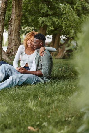Photo for Happy african american couple in casual wear hugging while sitting together on grass, romance - Royalty Free Image