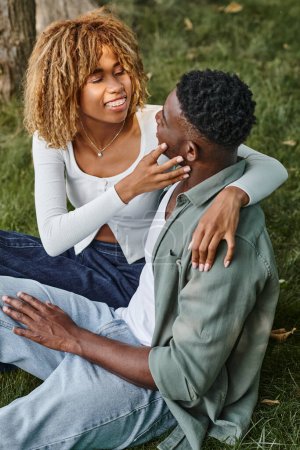 Photo for Happy african american woman in casual wear touching face of boyfriend and sitting on grass, banner - Royalty Free Image
