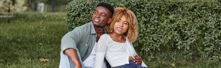 Photo for Cheerful african american couple hugging and sitting together on green grass, happiness banner - Royalty Free Image