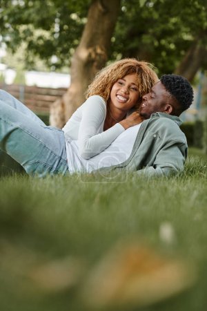 Téléchargez les photos : Heureux couple afro-américain ayant du temps de qualité avec l'autre tout en étant couché sur l'herbe - en image libre de droit