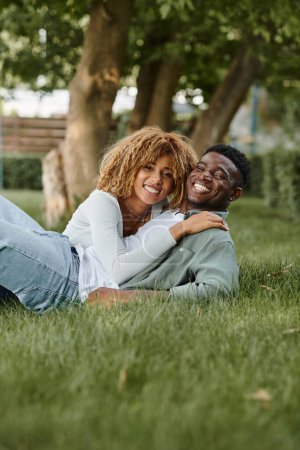 Téléchargez les photos : Heureux couple afro-américain ayant du temps de qualité avec l'autre tout en étant couché sur l'herbe - en image libre de droit