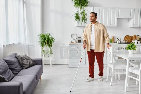 Téléchargez les photos : Attrayant aveugle homme indien dans casual confortable homewear en utilisant bâton de marche tout à la maison, handicapé - en image libre de droit