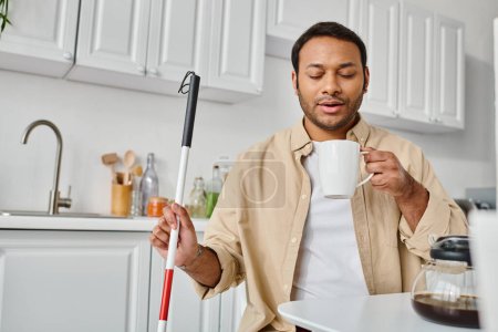 Photo for Attractive indian man with visual impairment sitting and drinking tasty coffee while on kitchen - Royalty Free Image