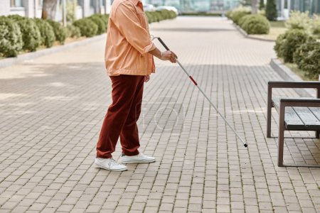 Photo for Cropped view of indian blind man in orange vibrant jacket using walking stick while outside - Royalty Free Image
