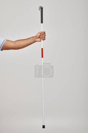 Photo for Cropped view of disabled indian man in blue tee shirt holding his walking stick on gray backdrop - Royalty Free Image