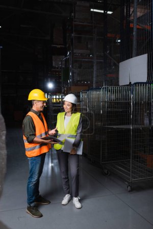 Photo for Two colleagues with hard hats standing in a well-lit warehouse, supervisor and employee - Royalty Free Image