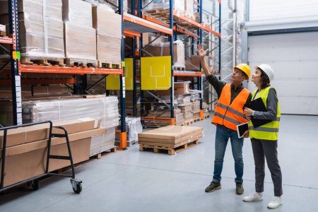 Photo for Cheerful supervisor with tablet pointing out details to female employee in a warehouse with cargo - Royalty Free Image