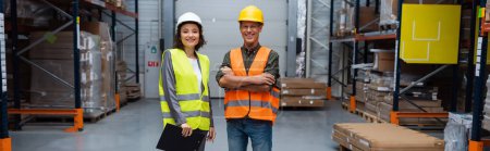 happy warehouse supervisor and employee in hard hats looking at camera, horizontal banner