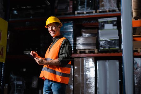 Photo for Happy middle aged warehouse supervisor in hard hat with clipboard, professional headshots - Royalty Free Image