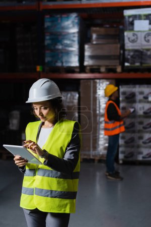 female warehouse employee in hard hat using table with a male colleague on blurred background