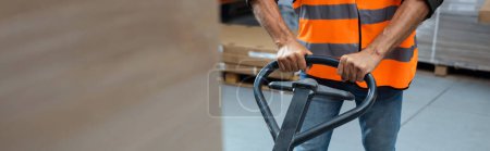 Photo for Cropped banner of warehouse worker in hard hat and safety vest transporting pallet with hand truck - Royalty Free Image