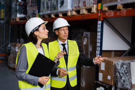 Photo for Warehouse supervisor instructing female employee in hard hat and safety vest, inspecting cargo - Royalty Free Image