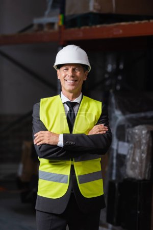 Smiling man in safety vest and hard hat standing with arms crossed, professional headshot