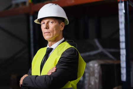 confident man in safety vest and hard hat standing with arms crossed, professional headshot
