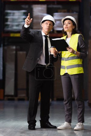 businessman in suit and hard hat planning logistics operations with female employee in safety vest