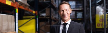 Photo for Happy middle aged businessman in suit smiling in warehouse, professional headshot banner - Royalty Free Image
