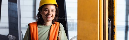 operador de carretilla elevadora femenina en sombrero duro y chaleco de seguridad sonriendo en el almacén, pancarta horizontal