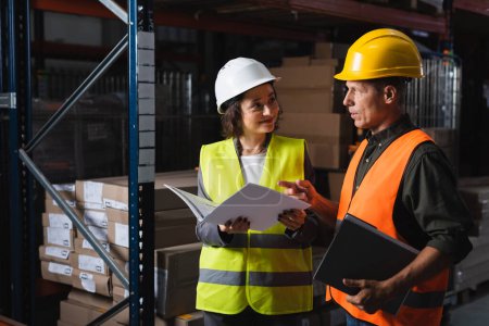 Two warehouse workers discussing logistics, happy middle aged man pointing at folder near woman