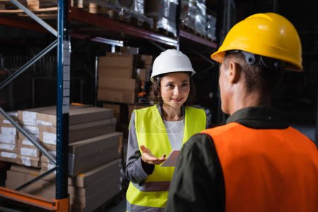 warehouse workers discussing logistics, cheerful woman with folder looking at middle aged colleague
