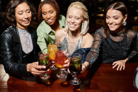 Téléchargez les photos : Excité multiculturel femmes amies cliquetis verres à cocktail pendant les loisirs dans le bar, plaisir - en image libre de droit