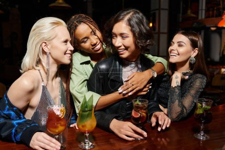 cheerful african american woman hugging asian girlfriend in cocktail bar, glamorous hen party